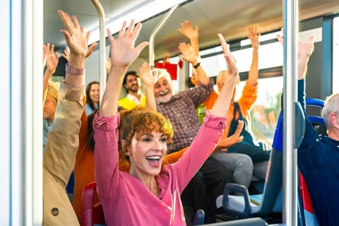 Diverse group of smiling passengers celebrating and cheering with arms raised inside a public
