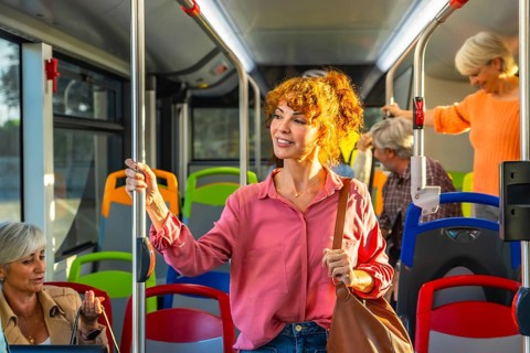 Woman standing on crowded city bus, holding a pole and smiling as she travels through the urban
