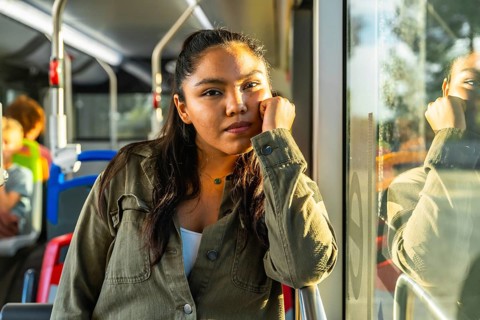 Young woman riding public transport contemplating and looking at camera while warm sunlight