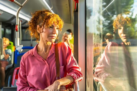 Curly red haired woman standing on a busy city bus during her commute, gazing thoughtfully out the