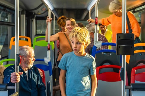 Young boy standing in a bus while other diverse passengers are commuting, experiencing urban public
