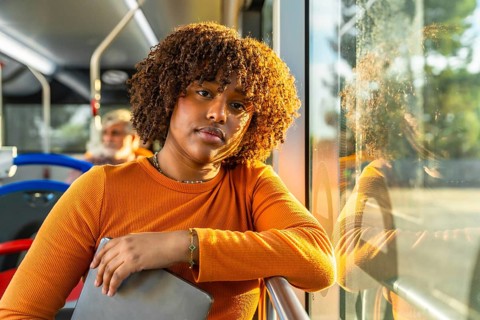 Young black woman with curly hair traveling on public transport, catching golden hour daylight