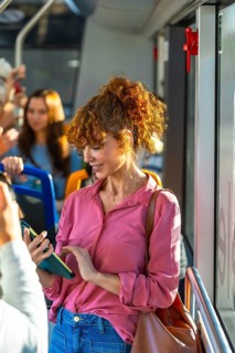 Young woman with red curly hair traveling by bus and checking her smartphone, connecting,