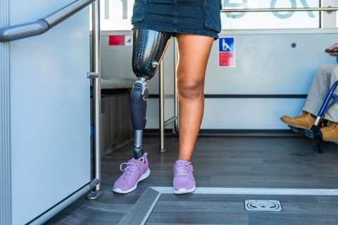 Amputee woman with a prosthetic leg and sneakers standing inside a bus, sharing the accessible