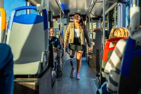 Young woman with a prosthetic leg confidently walking down a bright city bus aisle among seated