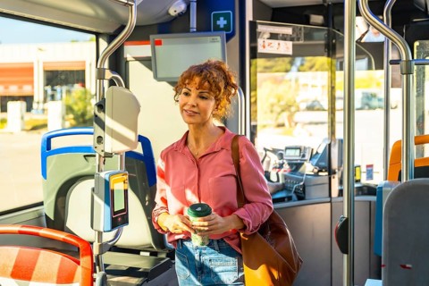 Woman standing on a city bus during the morning commute, holding a reusable coffee cup and brown