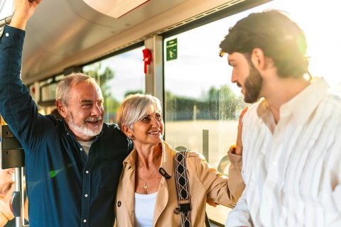Family generations chatting and smiling while standing on a bright city bus, sunlight streaming