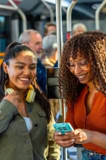 Two young adult women smiling and looking at a smartphone, enjoying public transportation while