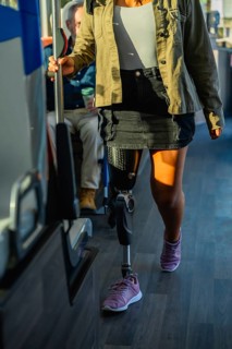 Woman with prosthetic leg and athletic shoe standing on a city bus, holding the handrail while