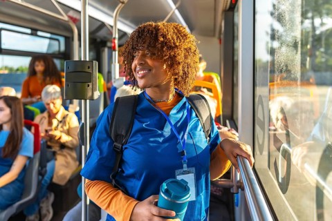 Smiling young black nursing student in blue scrubs with backpack and reusable cup, standing on a