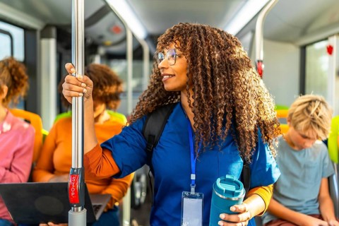 Healthcare professional with curly hair standing in a public transport bus, wearing scrubs while