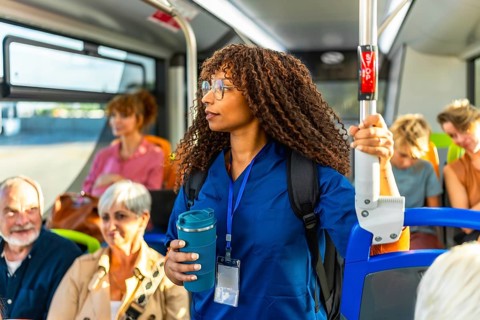 Young woman nurse in medical scrubs carrying a backpack and holding a reusable coffee cup,