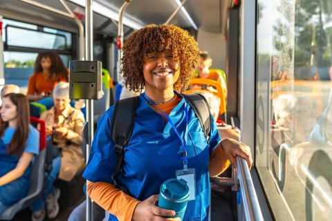 Young black woman doctor or student nurse standing on a public transport bus, wearing blue scrubs,