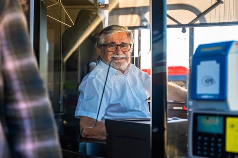 Mature man working as a bus driver, wearing glasses and a white uniform shirt, sitting inside the