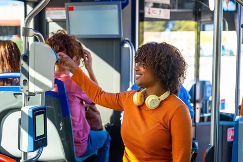 Smiling woman with headphones validating a contactless travel card on a modern electronic validator