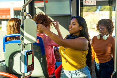 Young women traveling on a bus, smiling and interacting with a contactless payment ticketing