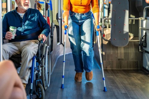Senior man in wheelchair and woman with crutches navigate a busy city bus aisle together,