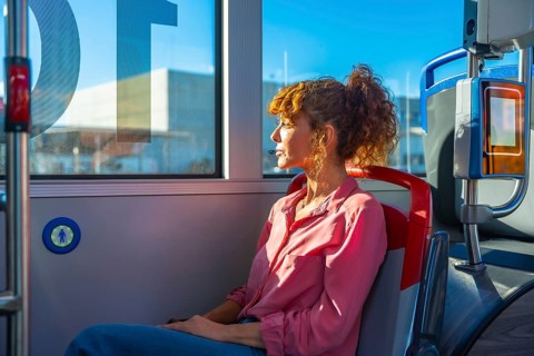 Woman seated on a city bus, gazing out the window in quiet thought during commute as sunlight