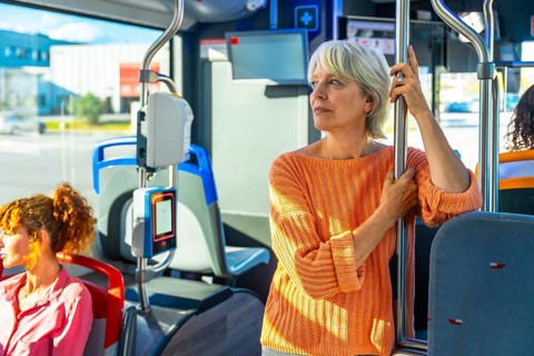 Senior woman standing on a public transport bus, holding a pole and looking out the window,