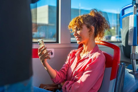 Woman on a city bus smiling while scrolling smartphone, enjoying digital content and staying