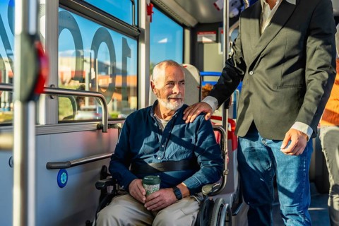 Senior man with a disability using public transportation, sitting in his wheelchair on a bus while