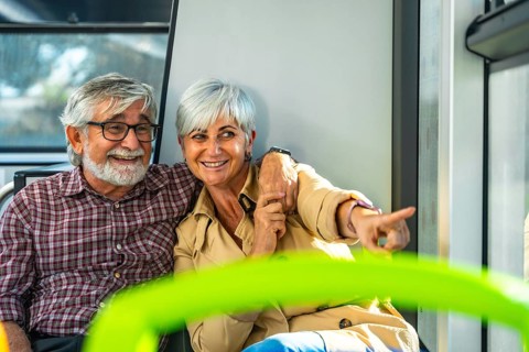 Happy senior couple on a bus, smiling and pointing out the window while enjoying a relaxed city