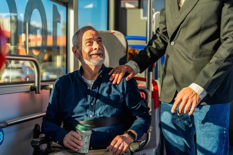 Young caregiver places hand on shoulder of smiling senior man in wheelchair during accessible