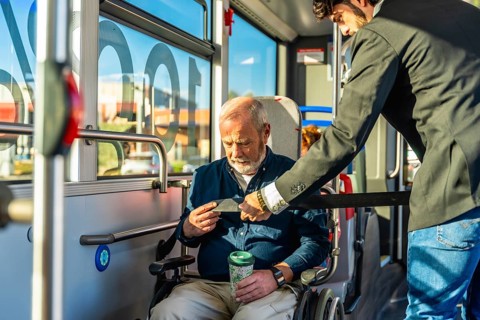 Younger man assisting a senior man in a wheelchair by securing his safety belt, ensuring