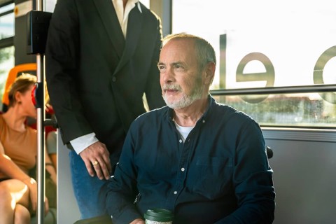 Senior man on a city bus, seated by the window with a reusable cup, gazing thoughtfully outside