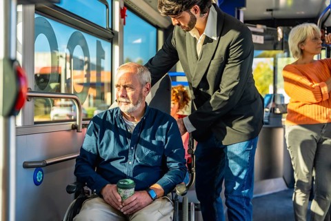 Young person assisting a senior man in a wheelchair on public transportation, ensuring