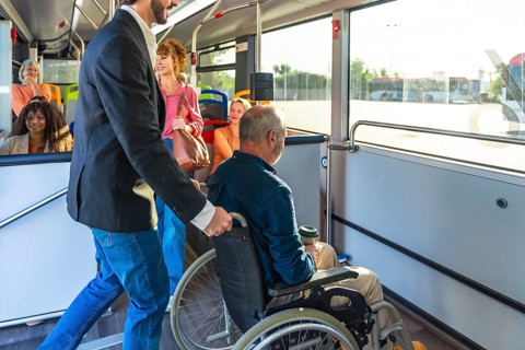 Man supporting a passenger in a wheelchair, providing assistance while boarding public transport,