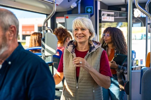 Senior woman smiling confidently, standing on a bustling urban bus alongside other passengers,