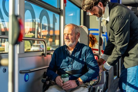 Employee assisting a senior man in a wheelchair on public transport, securing his position for a