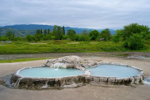 Hot spring pool in open landscape with wooded hills and mountains in the background, springs of