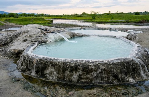 Hot spring pool in natural landscape with vast meadows and cloudy sky, springs of Amaghleba,