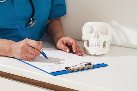 A medical professional reviews the patient's documentation, making notes. There is a model of a