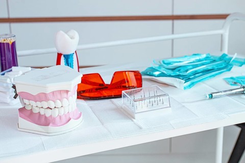 Various instruments, dental models, and hygiene items are laid out on the table in the dental