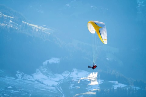 Paraglider flying over snowy mountains in winter in evening light, Kitzbühel Alps, Tyrol, Austria