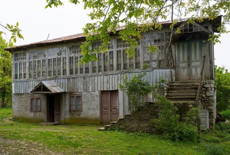 Old wooden house with lots of windows surrounded by trees in the countryside, Imereti region,