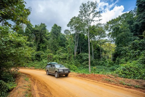 Toyota Hilux SUV drives on a dirt road through dense vegetation in tropical rainforest, Amani