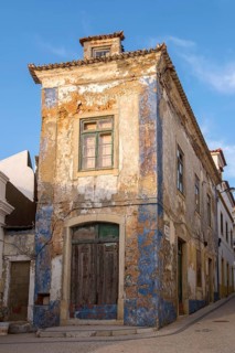 Abandoned building with peeling façade and blue paint residues under clear sky, Ericeira, Portugal