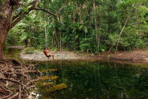 Man swings on a rope in the swimming pool at Emmagen Creek in Daintree National Park, Cape