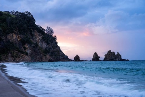 Landscape with sea, rocks and sandy beach in New Zealand in the evening at sunset. Otama Beach,