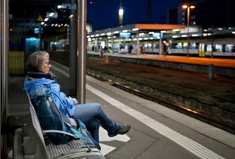 Night shot, elderly woman, traveler, sitting alone on a bench at the platform, backpack, main train
