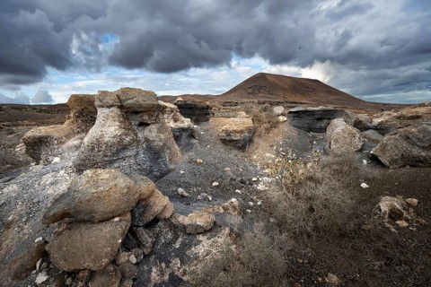 Eroded rock formations in volcanic landscape with dramatic cloudy skies, Ciudad Estratificada or