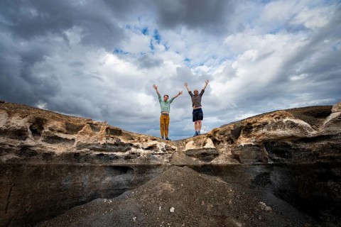 Two young men stretch their arms in the air, Eroded rock formations in volcanic landscape with