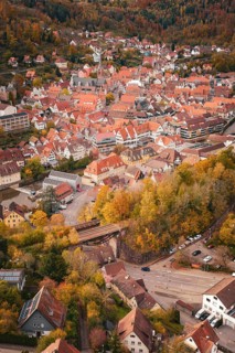 Panoramic view of a historic town with red-brick roofs and autumnal forest in the background, Calw,