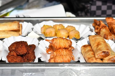 Various small fried Thai street food snacks like springrolls or potato noodle prawns on small trays