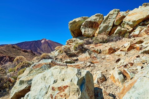Colorful rock in the foreground against a clear sky and a distant volcano, UNESCO World Heritage
