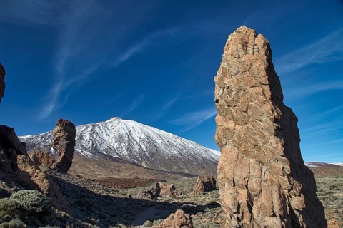 Snow-capped Teide, towering rock formations in front of a snow-capped mountain under clear skies,